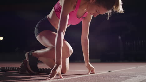 Female-athlete-training-at-running-track-in-the-dark-stadium.-Slow-motion.-A-young-female-athlete-gets-into-the-pads-and-starts-in-the-race.-close-up-of-a-girl-runner